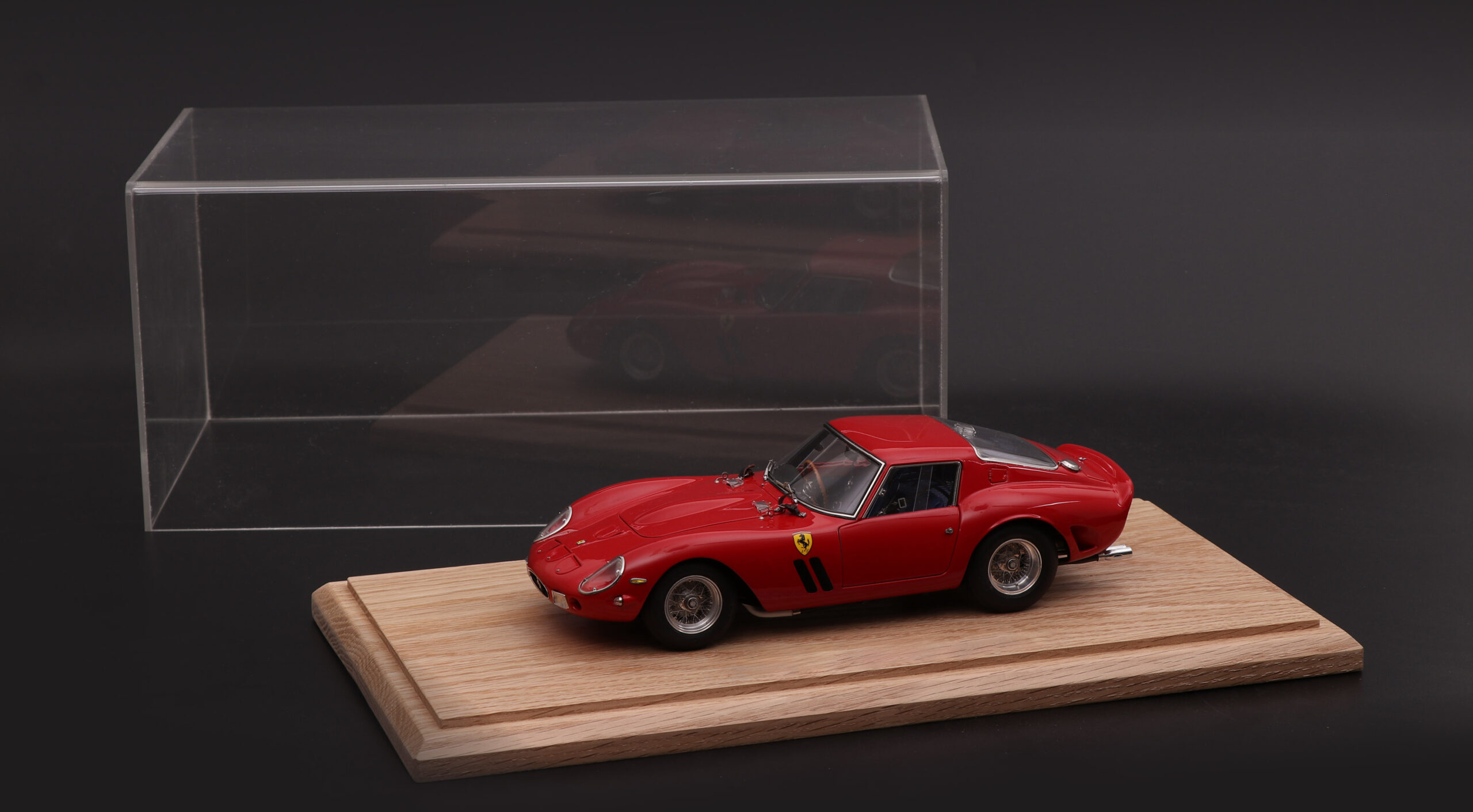 Red Ferrari model car beside its oak tabletop display case